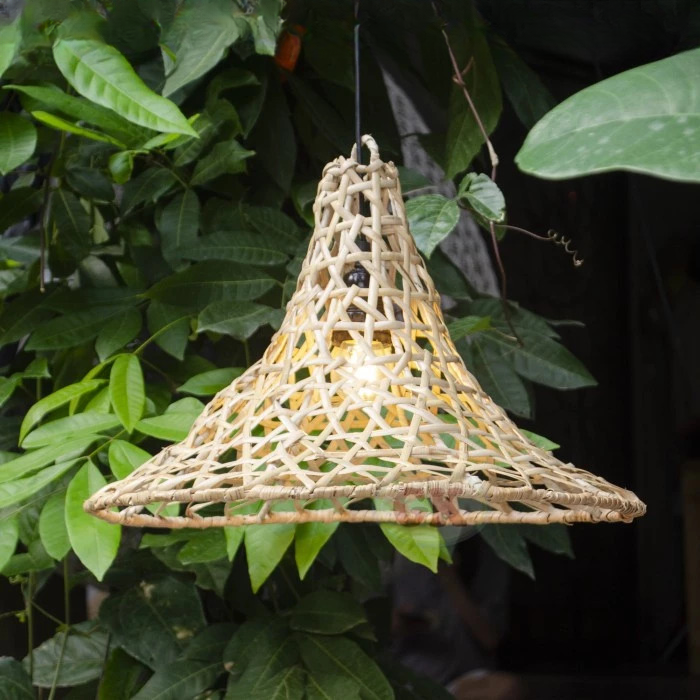 Petite suspension rotin forme conique présentée allumée devant des plantes